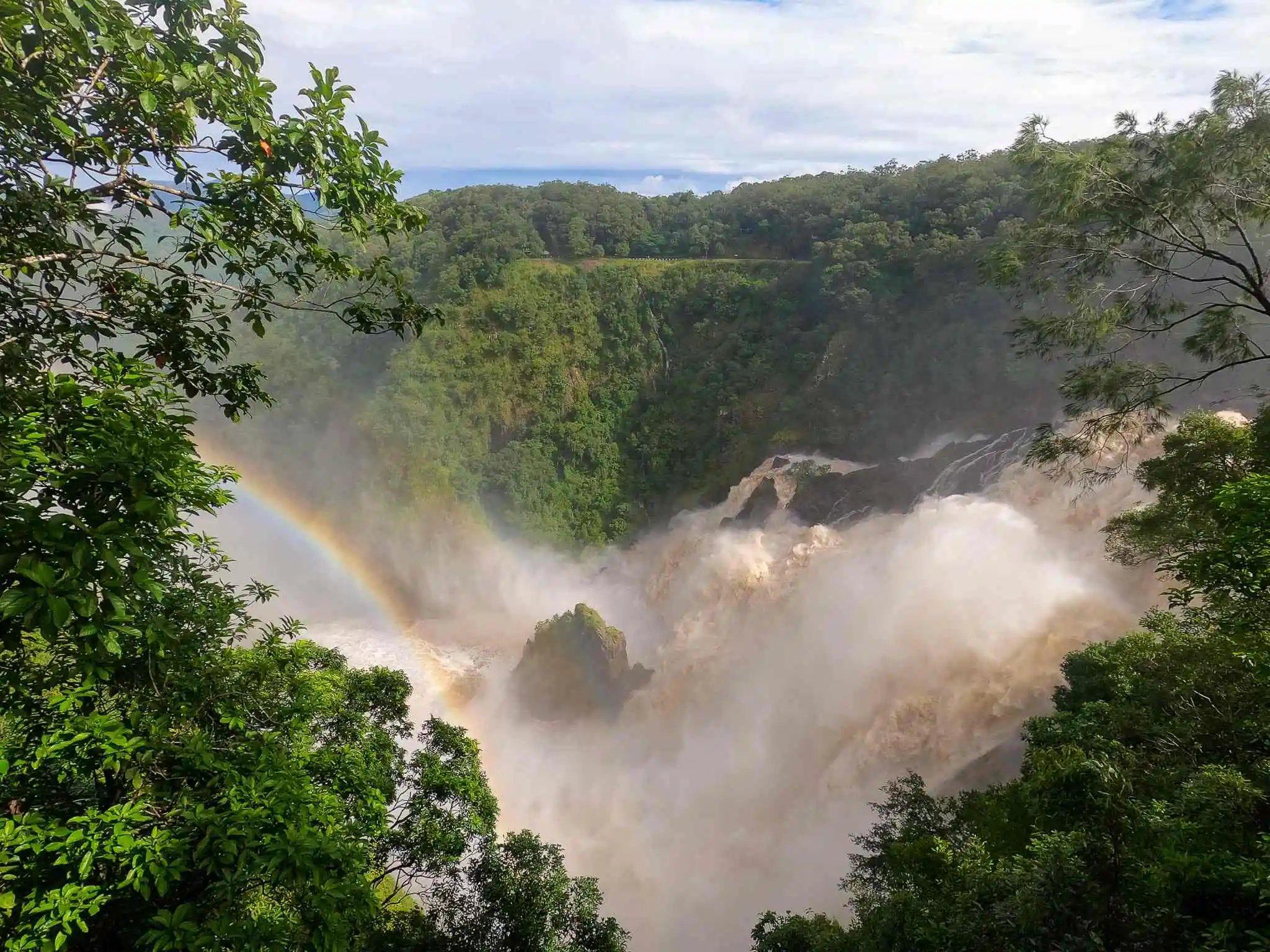 A powerful waterfall flows through a lush green rainforest into the deep gorge below with a rainbow