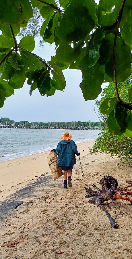 Ranger walking down the beach with her back to the camera picking up rubbish