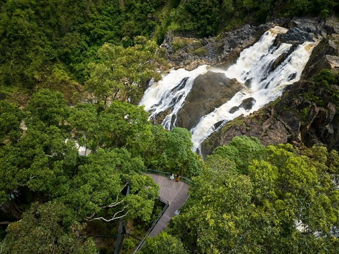 Looking down over Barron Falls, with the waterfall flowing heavily and two women watch from the Edge Lookout