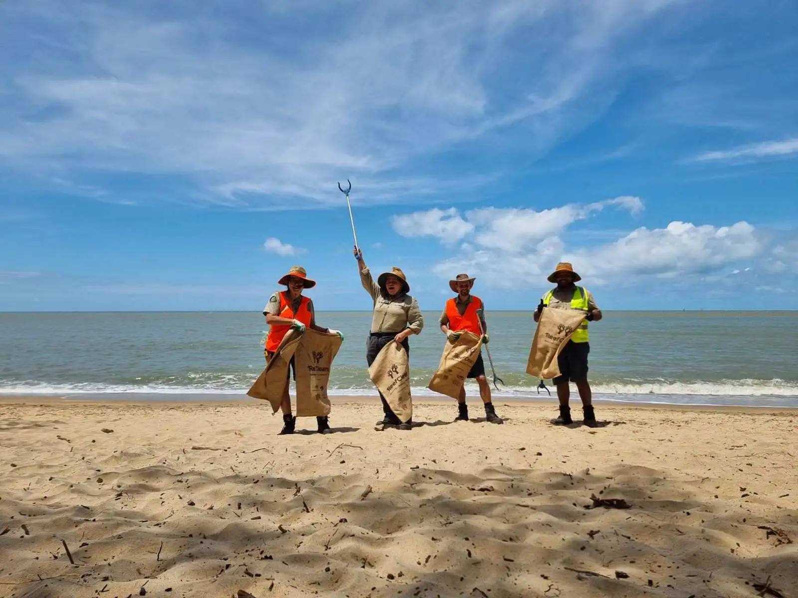 Four rangers stand proud on the beach with their rubbish sacks