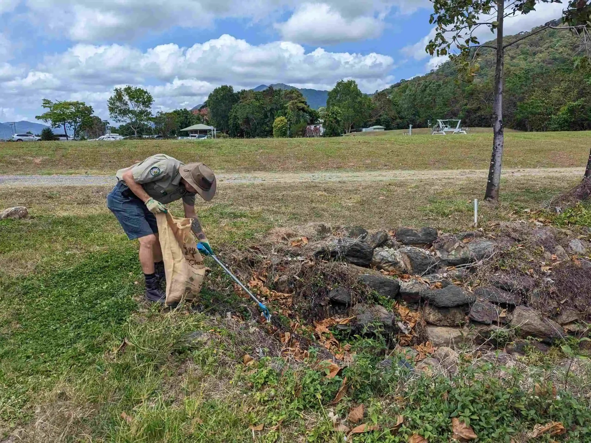 A Ranger holding a sack, leans over to collect rubbish with his picker