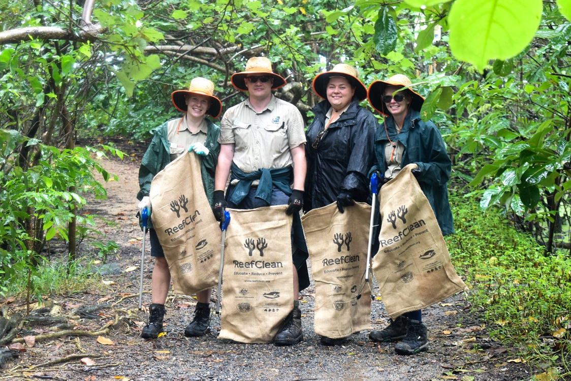 Skyrail Ranger team on a beach trail in the rain, all carrying large rubbish sacks