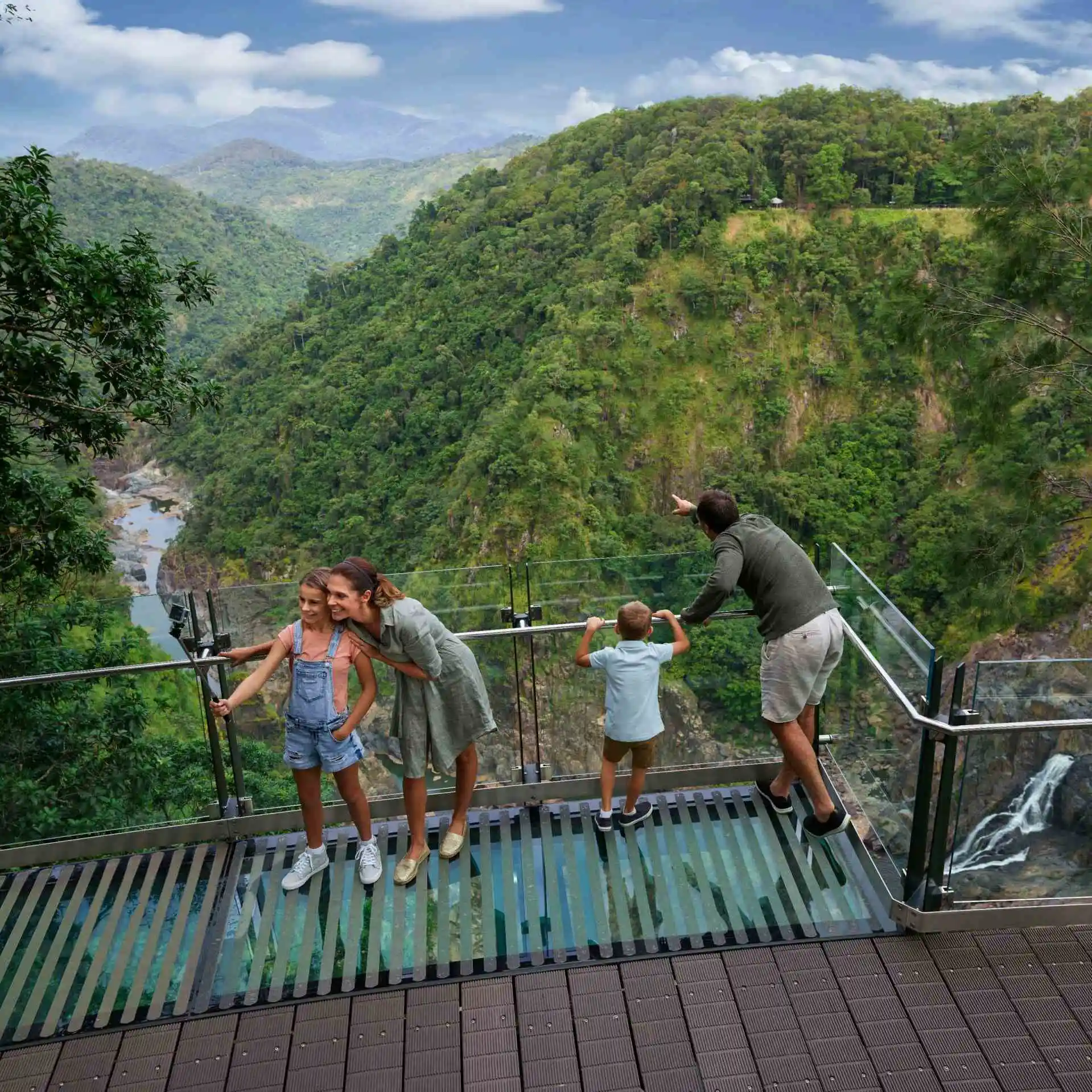 A woman and girls smile while taking a selfie. Behind them a man and boy look out into the deep gorge as they stand on a glass walkway and edge
