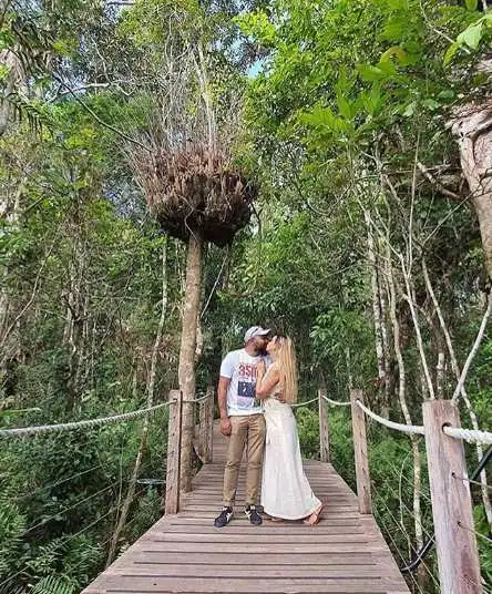 A male and female kiss on a wooden boardwalk surrounded by rainforest